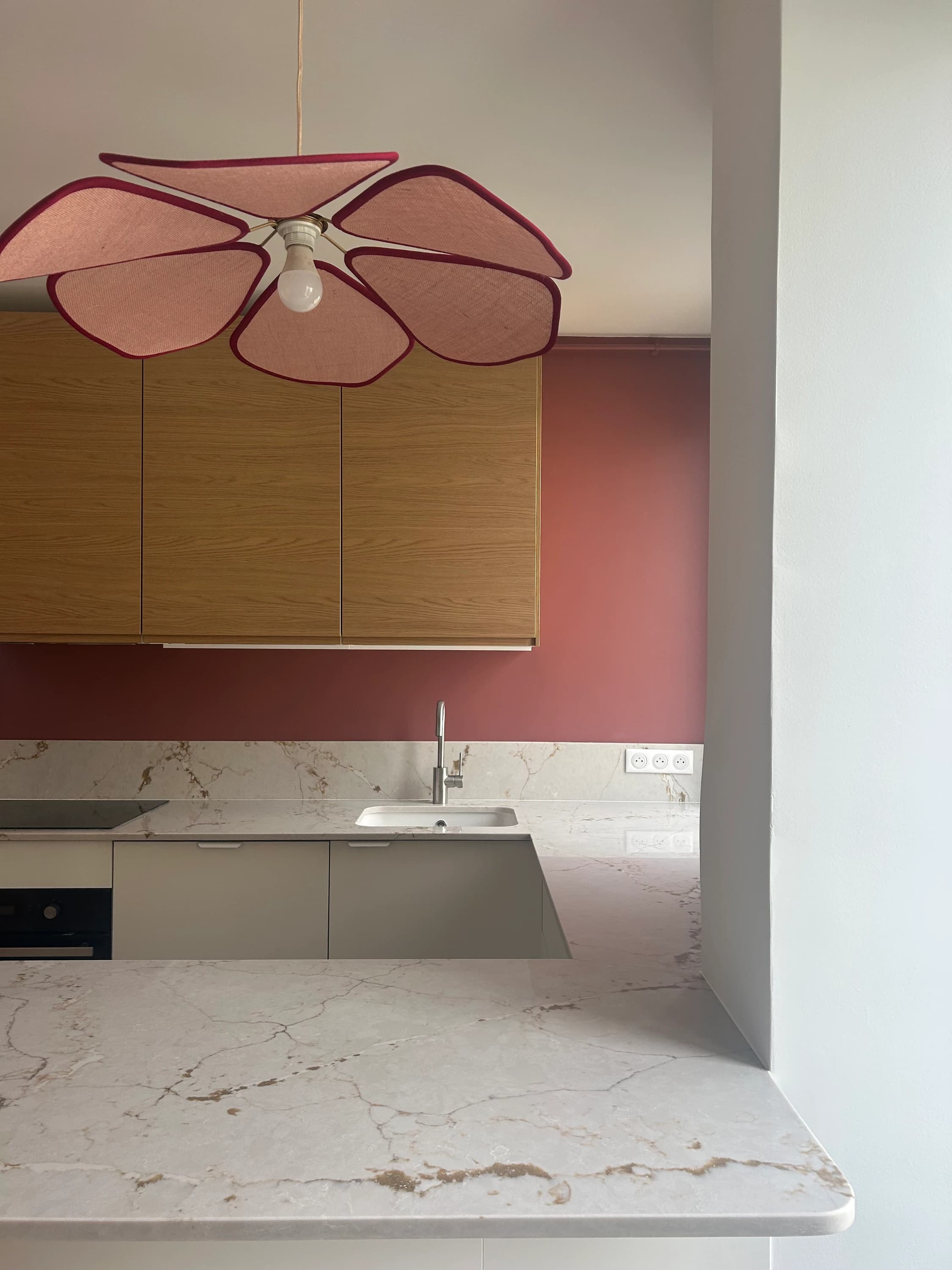 Cuisine ouverte sur mur framboise, plan de travail en pierre veinée et suspension en forme de fleur, appartement à Paris 16ᵉ